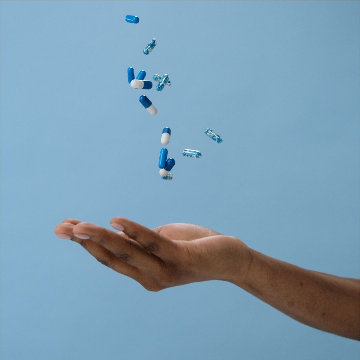 Hand showing blue supplements being thrown in the air.